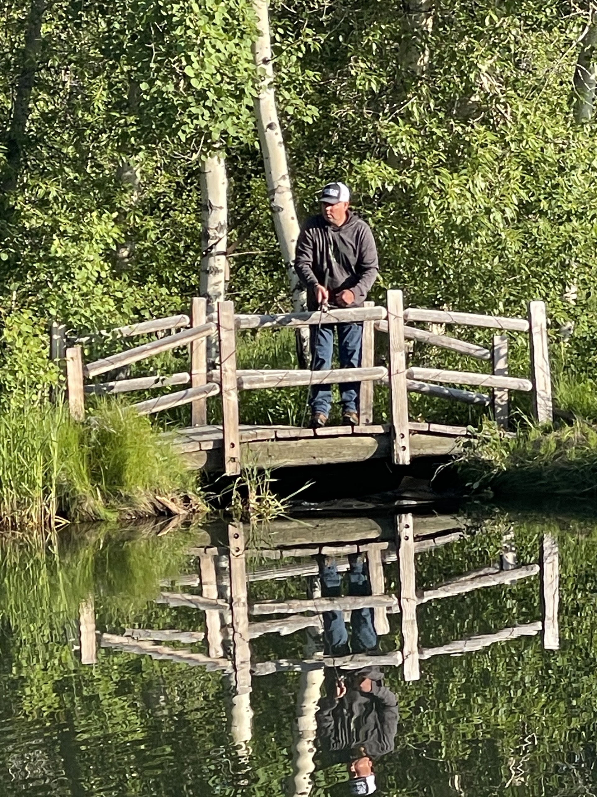 Anglers on a footbridge reflected in still water
