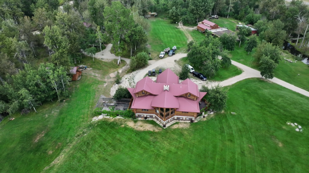Trucks sit parked near the lodge and along the looping drive, with a red-roofed outbuilding set back in the trees