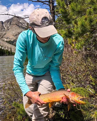 Angler with a brown trout and mountain backdrop