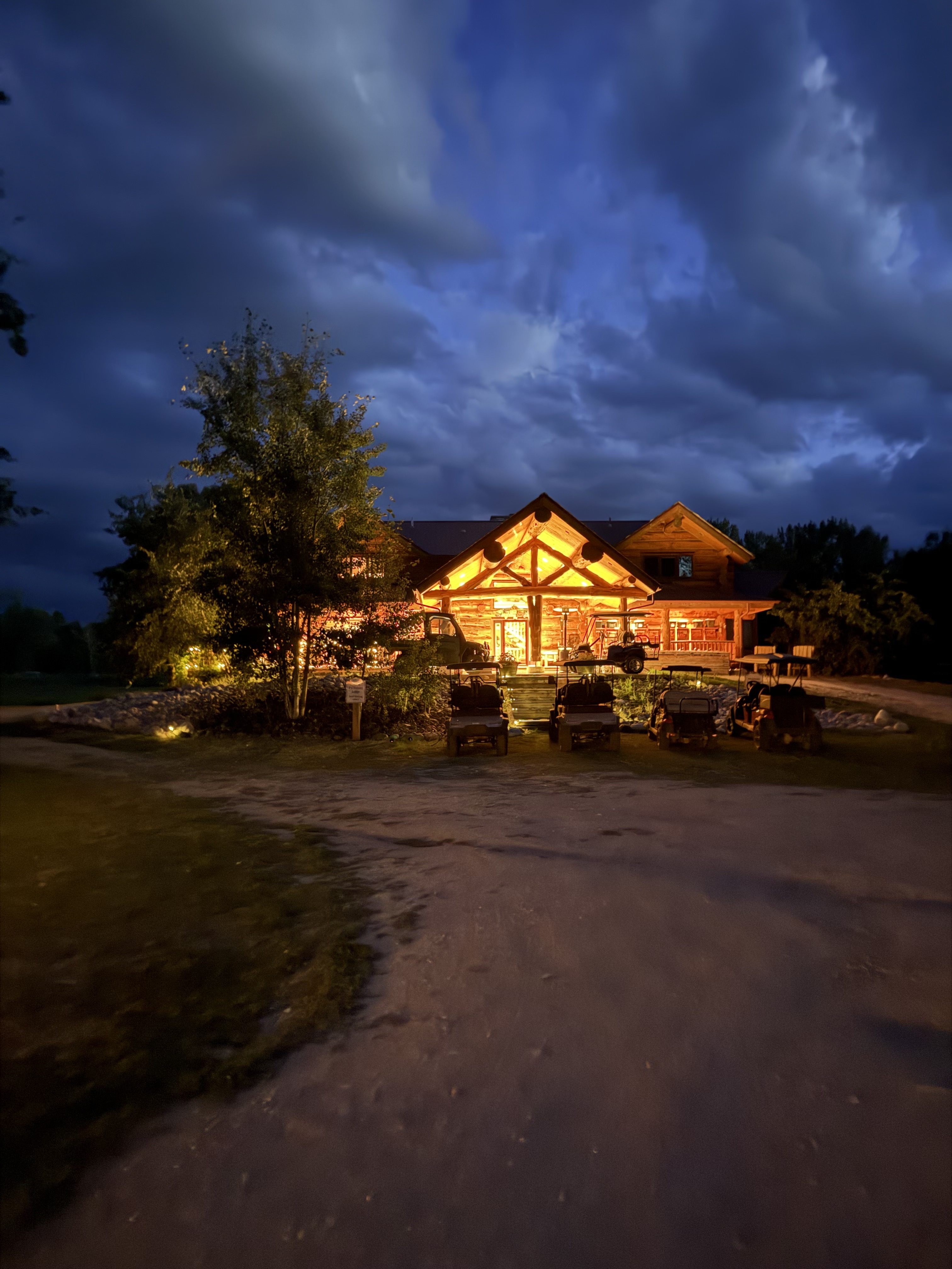 Golf carts lined up in the driveway as storm clouds roll over the log lodge, its entrance glowing warm at dusk