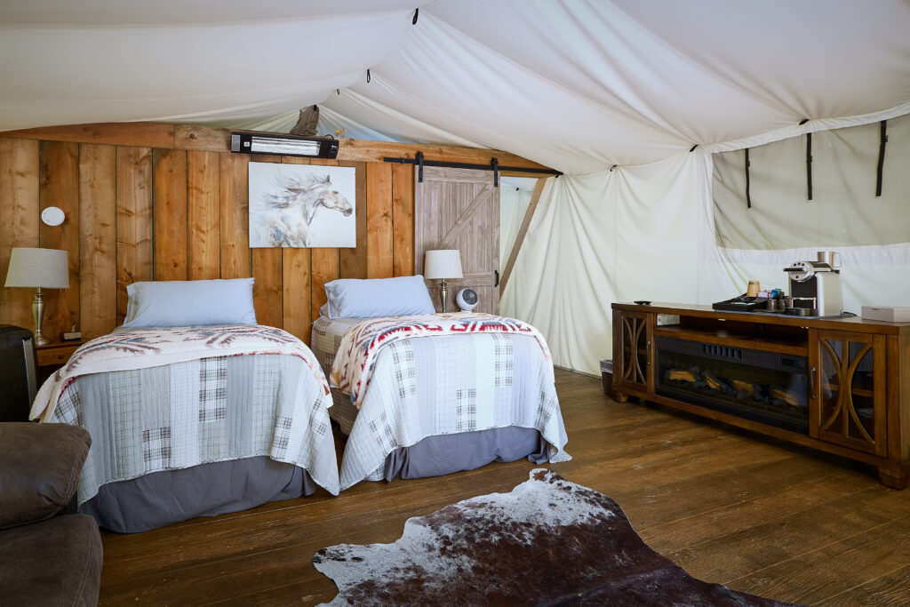Cowhide rug and wood credenza coffee bar beside twin beds with a horse painting on the wall in a canvas tent room