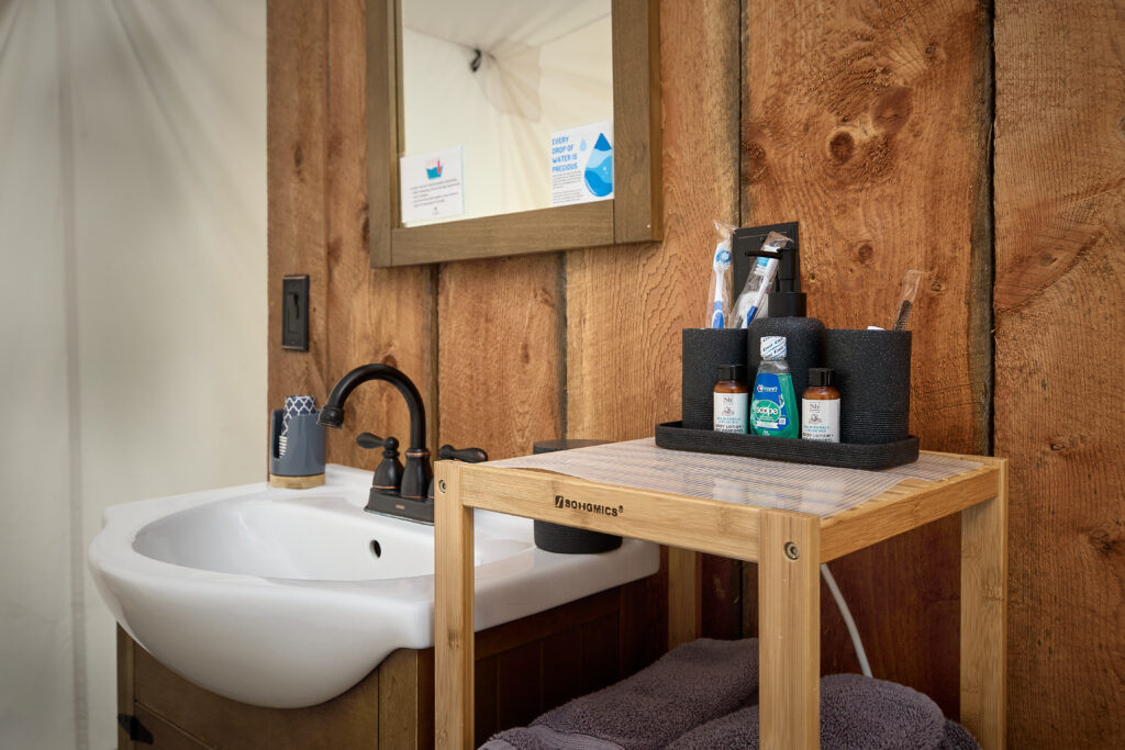 Oil-rubbed bronze faucet at the vanity sink, beside a wooden cart holding toiletries and folded towels