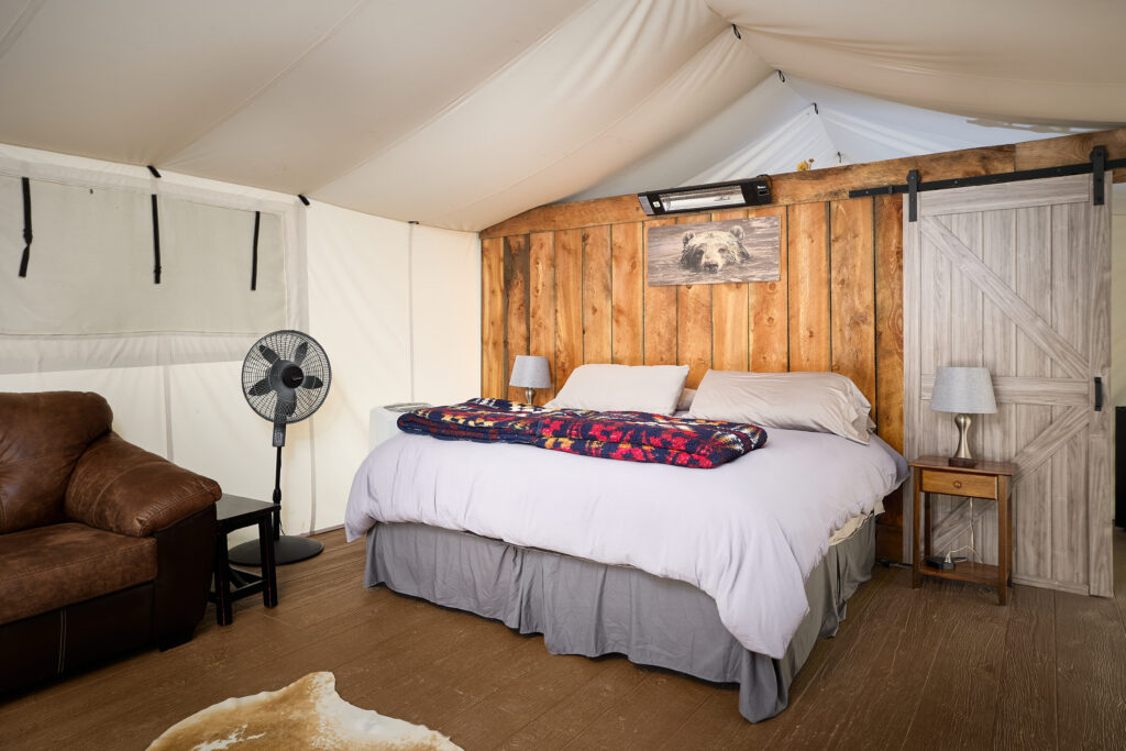 A king bed with white linens sits beneath a bear artwork, flanked by a leather sofa and an open barn-style door.