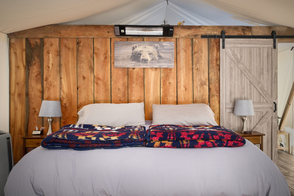 Bear photograph and sliding barn door beside a bed with folded Southwestern throws against a wood-plank wall