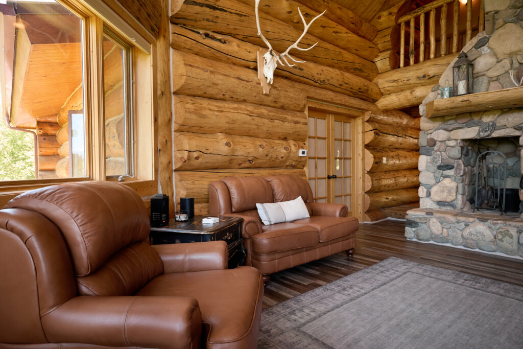 Leather loveseat and armchair beneath a mounted elk skull, near French doors and the stone fireplace in the log lounge.
