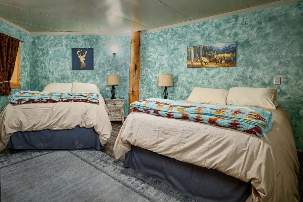 Two beds flank a rustic log support post beneath teal textured walls hung with deer and elk artwork