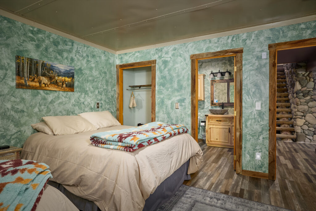Elk canvas print above the bed, with doorways opening to a vessel-sink bathroom and a river-stone staircase landing