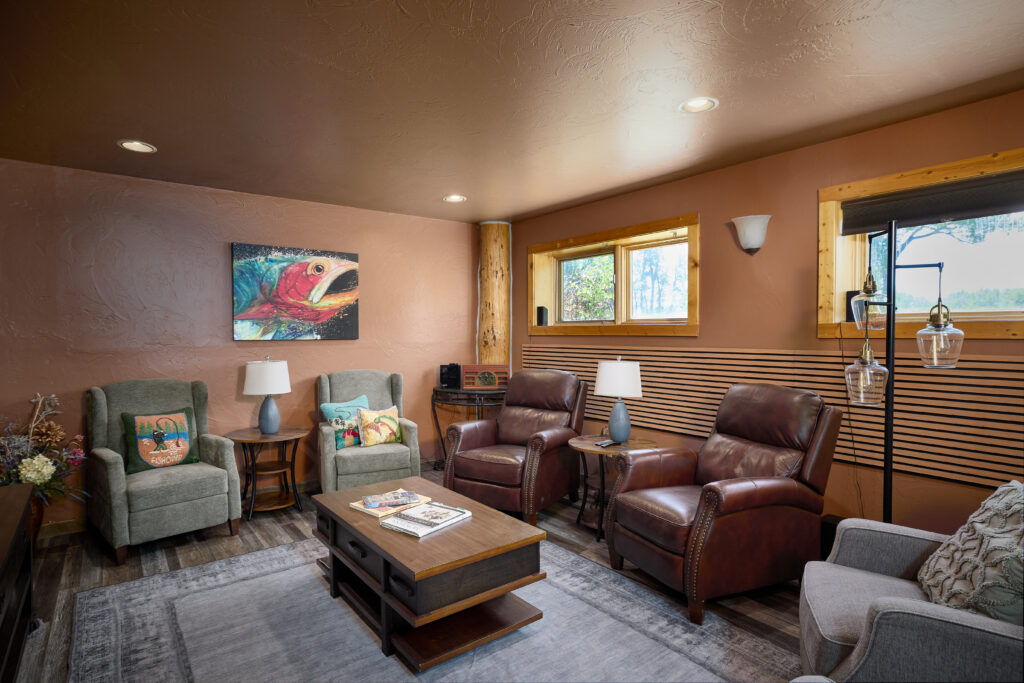 A cozy lounge with leather recliners, patterned armchairs, and a fish painting overlooking wooded windows.