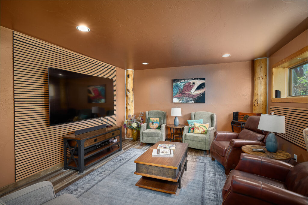 A den with a large mounted television on a slatted wood accent wall, leather recliners, and log support beams.
