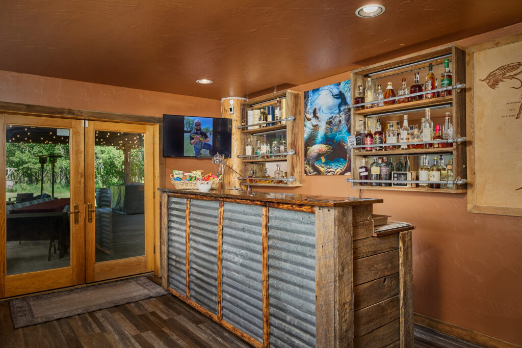 A rustic wet bar with corrugated-metal paneling, stocked liquor shelves, and French doors opening to the patio.