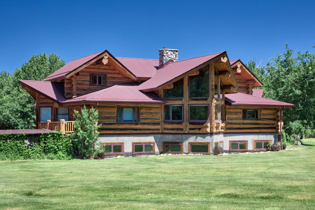 A close view of the lodge's log construction and towering great-room windows, with a stone chimney