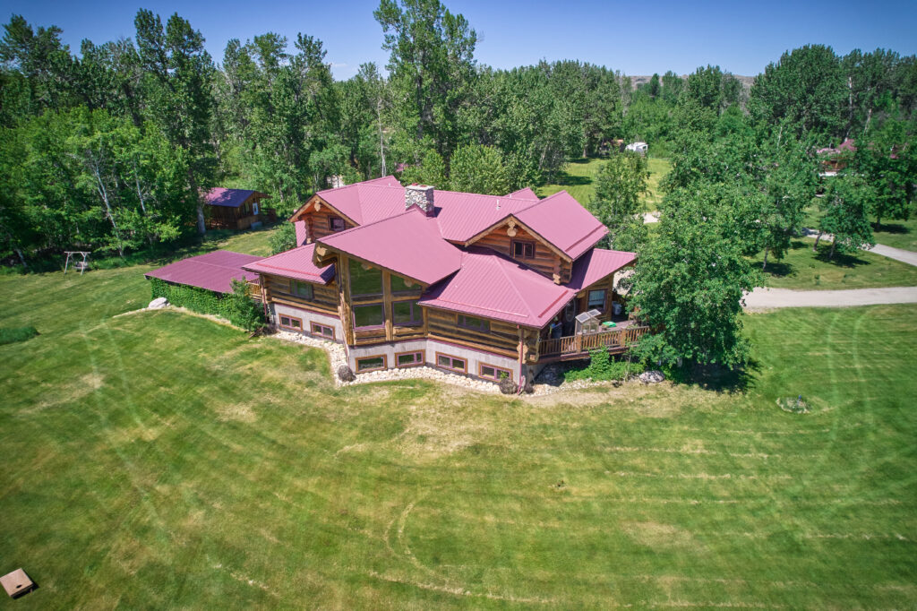 Multi-gabled red metal roofline and log construction of the lodge, ringed by mature trees with a guest cabin nearby