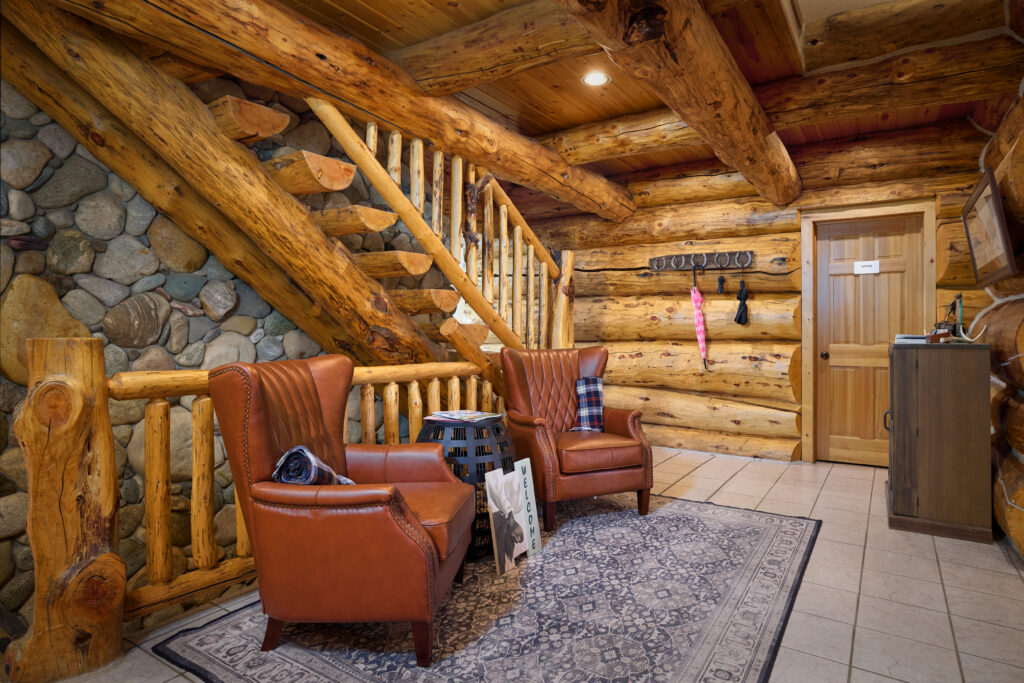 Log cabin lobby with leather wingback chairs beside a river-stone and log staircase