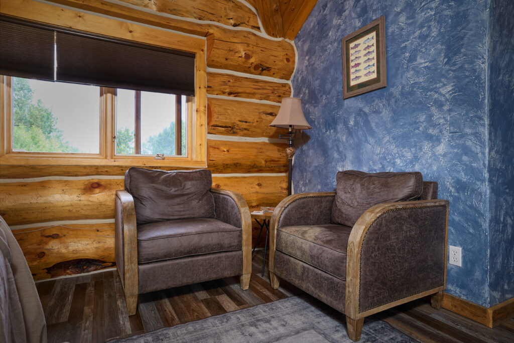 A bedroom sitting nook with two leather armchairs and a framed fish print against a blue textured wall