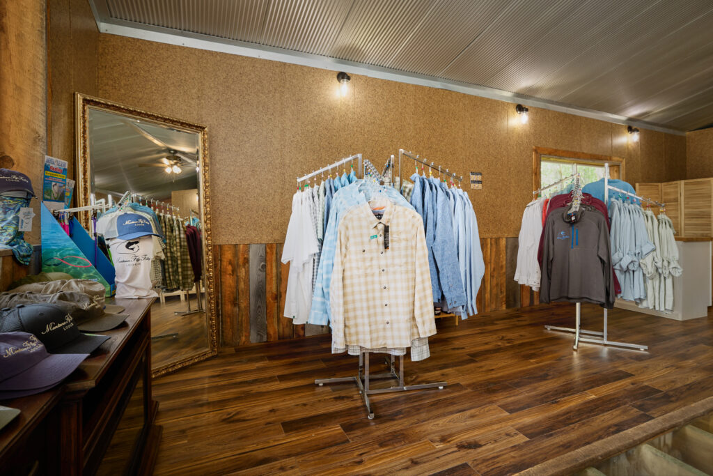 Fishing shirts hang on display racks inside the lodge's fly shop, with hats arranged on a wooden table