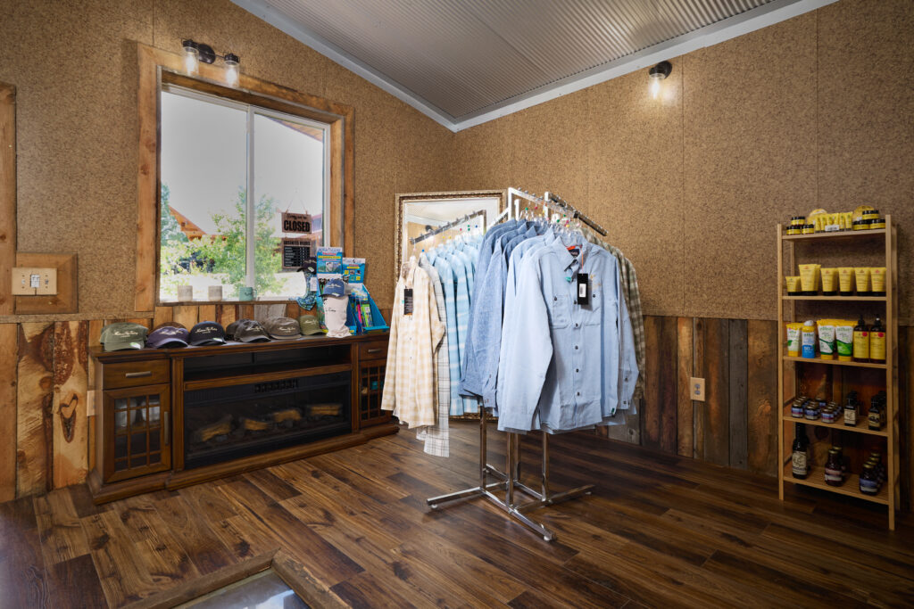 Pro shop display of button-down fishing shirts on a rack beside a stone fireplace console and ball caps