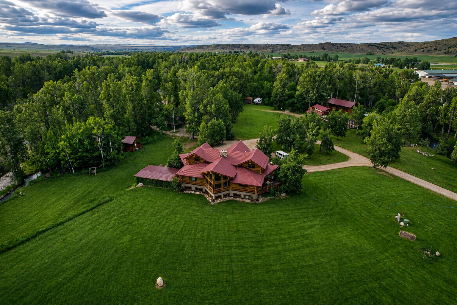 Rolling foothills and a dramatic sky frame the log lodge and outbuildings across a wide mown lawn